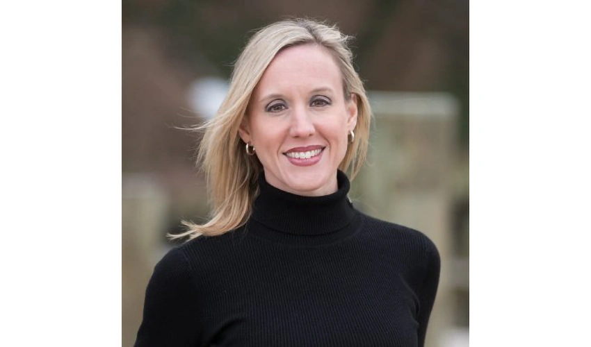 photo of a blonde, light skinned woman in a dark turtleneck looking at the camera